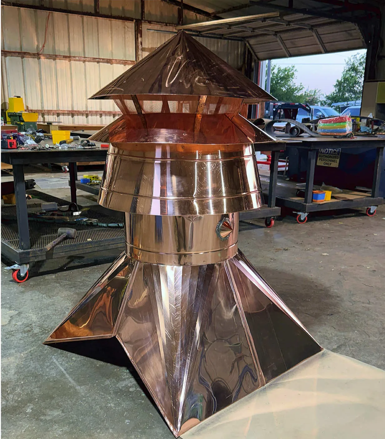 Large fabricated copper chimney cap with a hipped lid and tapered base on the shop floor