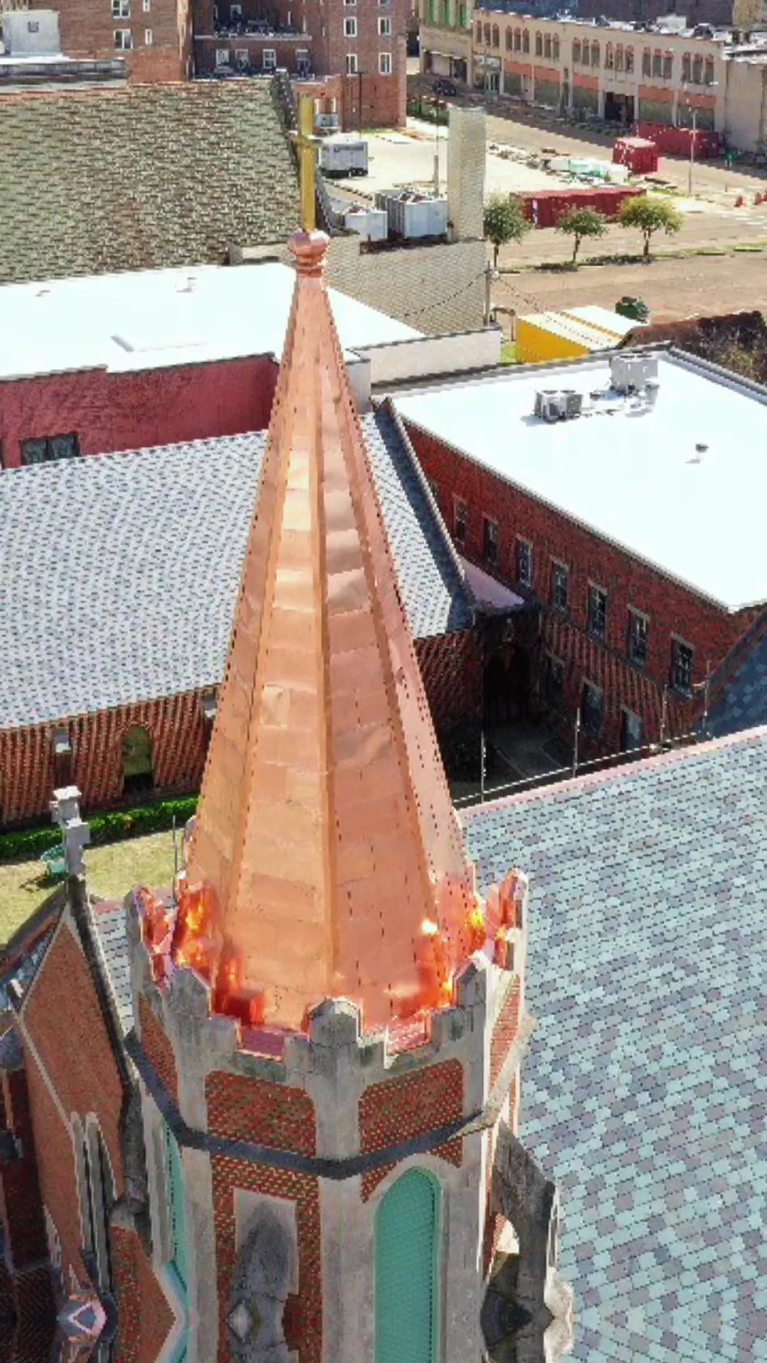 Aerial view of a church steeple re-clad in new copper, rising above the rooftops of a town