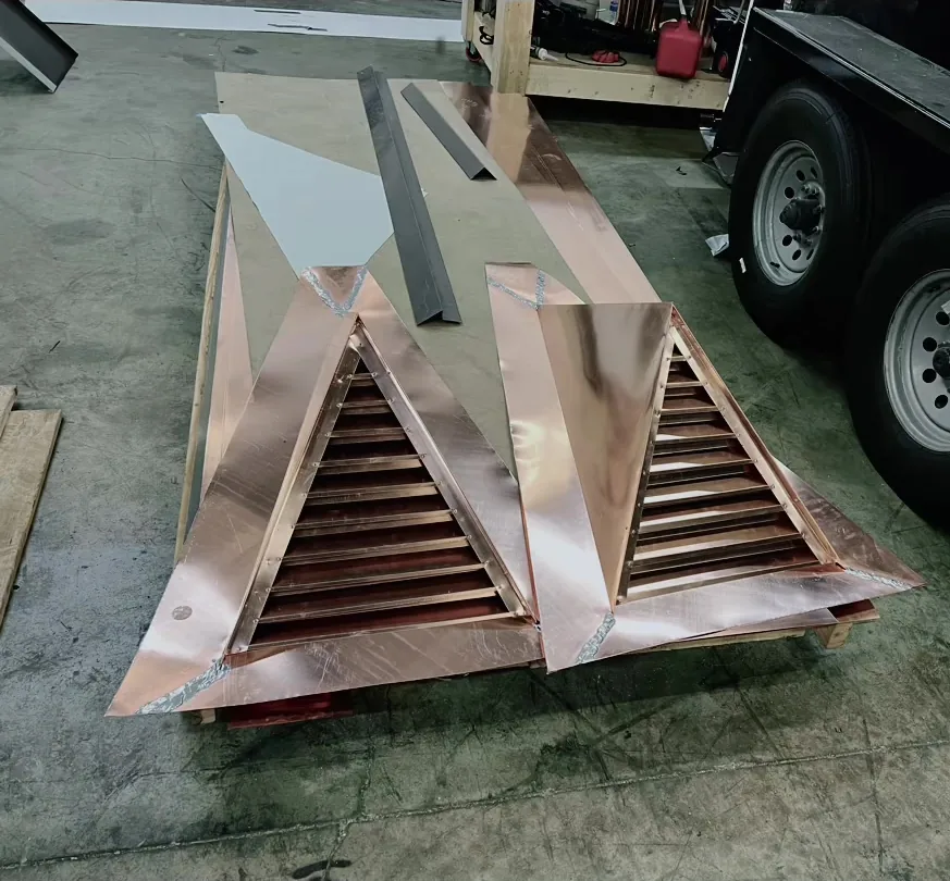Two triangular copper gable louvers with fixed blades, loaded on a trailer at the shop