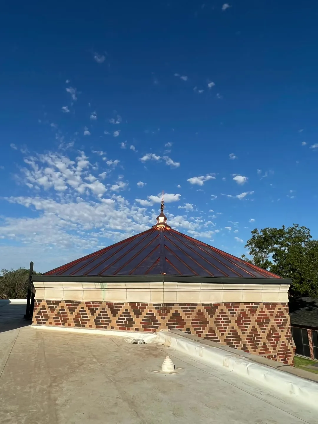 Pyramid roof clad in new, bright copper with a diamond-pattern copper band, on a flat commercial roof under a blue sky