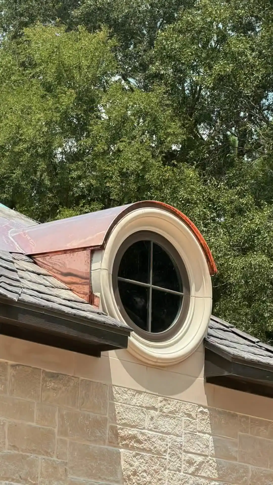 Round dormer window wrapped in new copper on a slate roof above a stone wall